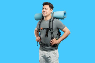Sırt çantası ve paspas takan mutlu Asyalı adam gülümsüyor ve maceraya hazır bekliyor.