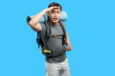 Sırt çantalı genç bir adam uzaktaki mesafeye bakıyor gözlerini koruyor.