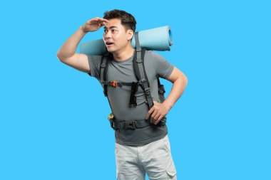 Yürüyüşçü, parlak mavi bir arka planda sırt çantası ve kargo şortuyla gözlerini koruyor.