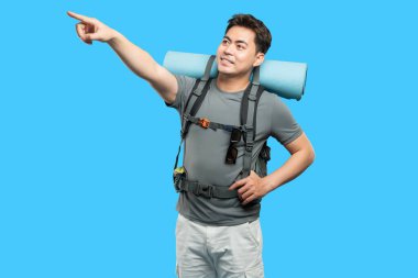 Sırt çantalı genç gezgin mavi arka plandaki bir şeyi işaret ediyor.