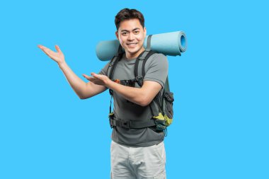 Sırt çantası ve uyku paspası takmış gülümseyen bir erkek yürüyüşçü boş bir uzay stüdyo çekimine doğru hareket ediyor.