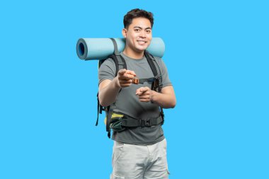 Sırt çantalı gülümseyen Asyalı yürüyüşçü, maceraya hazır. Seyirciye coşkuyla işaret ediyor.