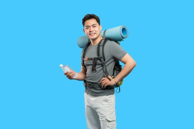 Açık hava macerasına hazır aktif bir yürüyüşçü elinde su şişesiyle kamp malzemelerini taşıyor.