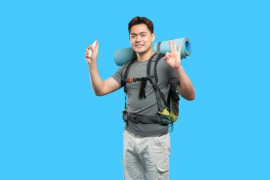 Yürüyüşe hazır gülümseyen bir sırt çantası spreyi tutar ve açık mavi arka planda 