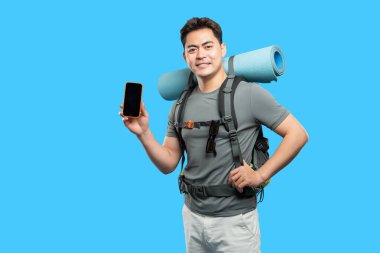 Gülümseyen yürüyüşçü mavi arka planda uyku tulumlu sırt çantası takan bir akıllı telefonu görüntüler.