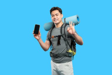 Sırt çantasıyla gezmeye hazır gülümseyen Asyalı adam elinde telefonla 