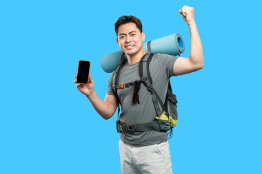 Sırt çantalı Asyalı bir adam, yürüyüşü sırasında başarılı bir navigasyon ya da bağlantı olduğunu gösteren telefonunu neşeyle sergiliyor.