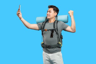 Heyecanlı bir yürüyüşçü macera için sırt çantasıyla gezer ve parlak bir arkaplan ile selfie çeker.