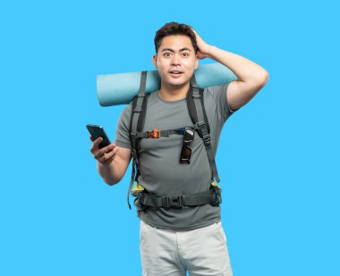 Şaşırmış bir yürüyüşçü, kamp malzemeleriyle sırt çantası takıp telefondan yön sorar.