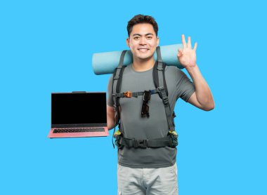 Gülümseyen yürüyüşçü, stüdyo ortamında dizüstü bilgisayarlı açık mavi bir sırt çantası takarken iyi niyet gösteriyor.