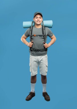 Sırt çantasıyla bir stüdyoda poz veren bir yürüyüşçünün mavi arka planda tam pozu.