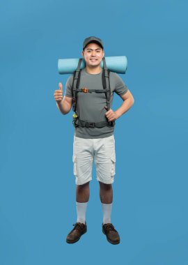 Sırt çantası takan bir adam yürüyüşe hazırdır. Kamp malzemeleriyle başparmağını kaldırır.