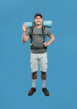 Sırt çantasında beysbol şapkası ve beyaz şortuyla gülümseyen yürüyüşçü, tamam işareti veriyor.