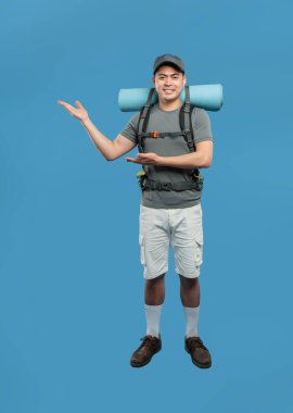 Hevesli yürüyüşçü sunuyor ve keşfetmeye hazır mavi bir arka planda açık hava kıyafeti giyiyor.