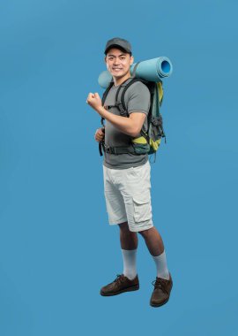 Sırt çantası taşıyan ve mavi hasırda yuvarlanan günlük kıyafetler giyen gülümseyen bir erkek yürüyüşçünün tam karesi.