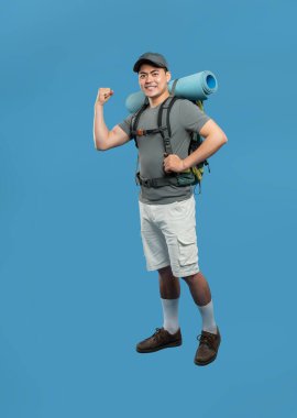 Sırt çantası ve uyku tulumuyla maceraya hazır gülümseyen bir adam pazılarını esnetir.