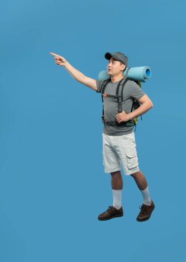 Sırt çantalı bir erkek yürüyüşçü parlak mavi bir arka plana karşı duruyor.