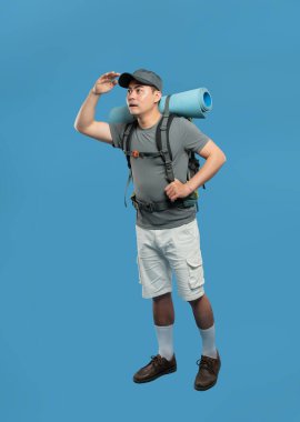 Yürüyüş kıyafeti giyen bir adam gözlerini koyu mavi bir arka plana gölgeleyerek mesafeye bakar.