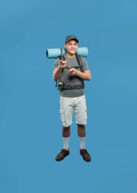 Yürüyüş için giyinmiş hevesli bir adam mavi arka planda mavi bir sırt çantası ve mavi bir yastıkla