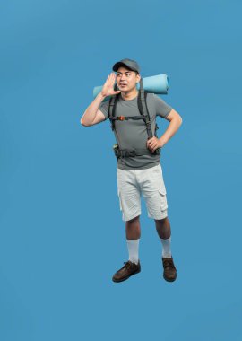 Sırt çantalı bir yürüyüşçü mavi arka planda duyulmak için elini ağzına dayayıp bağırıyor.