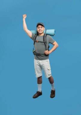 Sırt çantası ve uyku paspası olan mutlu erkek yürüyüşçü avucunu kaldırıyor ve maceraya hazır bir şekilde gülümsüyor.