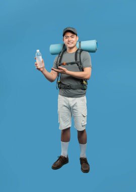 Yürüyüş kıyafeti giyen bir adam sırt çantası ve şapkası olan mavi bir arka planda su şişesi tutan bir adam.