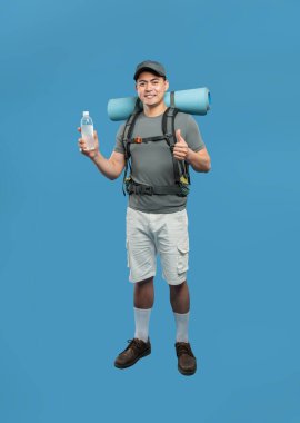 Sırt çantalı gülümseyen bir adam mavi zemin üzerinde su tutarken baş parmağını kaldırır. Yürüyüşe çıkmaya hazır.