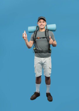 Sırt çantalı bir yürüyüşçü mavi bir zeminde durur ve koruma için yürüyüşe çıkmadan önce püskürtücü sıkar.