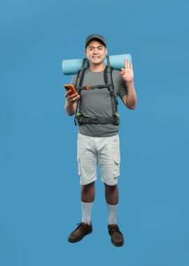 Yürüyüş takımlı, sırt çantalı ve şapkalı bir adam telefonuna bakarken gülümsüyor. Mavi arka planda 