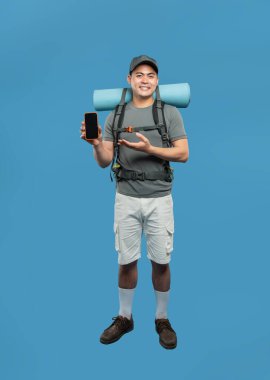 Şapka tişörtlü ve şortlu bir adam arka planda izole edilmiş bir kamp paspası olan bir telefon tutuyor.