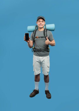 Sırt çantalı ateşli yürüyüşçü mavi arkaplanda telefon gösterilirken baş parmağını kaldırıyor.