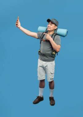 Yürüyüş kıyafetleri içinde tutkulu bir adam mavi arka planda bir selfie çeker macera ruhunu yakalar