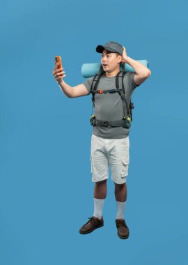 Adamın biri telefonuna sırt çantasıyla bakıyor. Yüzünde bir şok ifadesi var. Mavi fon.