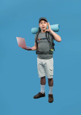 Mavi arka planda bir yürüyüşçü dizüstü bilgisayar tutuyor ve dikkatle sırt çantası takıp yürüyüş takımlarını dinliyor.