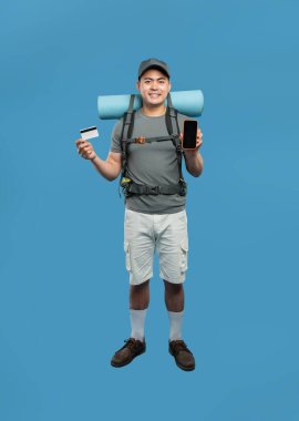 Mavi arka planda, elinde bir kart ve telefon ile gezintiye çıkmaya hazır bir erkek sırt çantasının tam karesi.