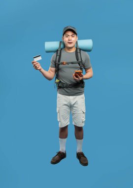 Hevesli yürüyüşçü, mavi arka planda telefon ve kredi kartı tutarak maceraya hazır.