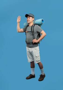 Sırt çantalı ve hasırlı gülümseyen bir adam. Merhaba mavi bir fon üzerinde maceraya hazır.