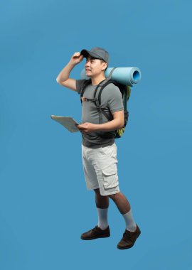 Sırt çantası ve haritası olan bir erkek yürüyüşçü mavi arka planda uzaklara bakmak için mola verir.