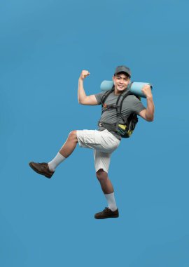 Hevesli bir yürüyüşçü, zaferle yumruklarını sallar ve başarısını sırt çantası ve mavi arka planla ifade eder.