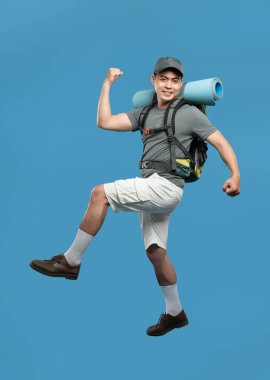 Aktif kıyafet ve kamp örtüsü içinde neşeli bir yürüyüşçü mavi arka plana karşı zafer pozu veriyor.