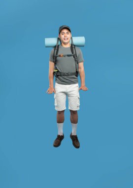 Sırt çantalı bir adam, şapkasıyla gezmek için mavi bir arka plana atlıyor.