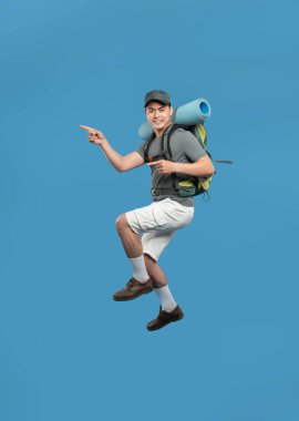 Neşeli bir yürüyüşçü sırt çantasıyla sırt çantasına atlayıp açık hava yolculuğuna doğru neşeyle işaret eder.