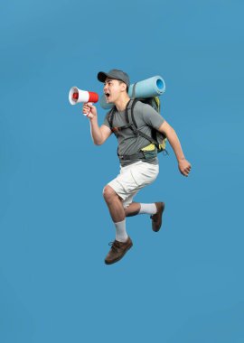 Sırt çantalı genç bir Asyalı, mavi arka planda kırmızı ve beyaz bir megafona atlıyor.