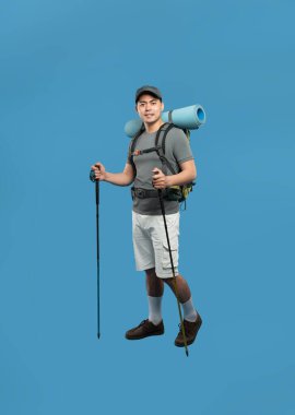 Sırt çantalı ve bastonlu gülümseyen Asyalı adamın tam pozu mavi arka planda hazır.