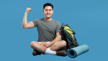 Atletik bir adam sırt çantasıyla pazılarını esneterek oturur ve yanına paspas serer.