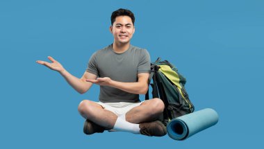 Sıradan giyinmiş gülümseyen Asyalı bir adam açık hava seyahat takımlarına doğru hareket ediyor. Macera bekliyor.!