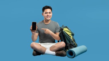 Sırt çantalı bir adam akıllı telefonu işaret ederek açık hava macerasına ve online gezi planlamaya hazır.