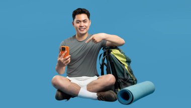 Gülümseyen adam açık hava macerasına hazırlanırken sırt çantasını ve yoga minderini gösteriyor.