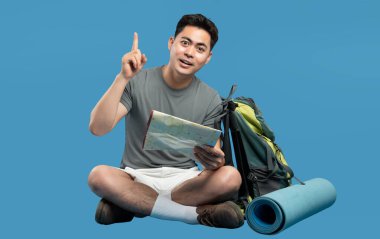 Heyecanlı bir yürüyüşçü mavi bir arkaplanda oturur, seyahat takımları ve işaret eden bir haritayla.