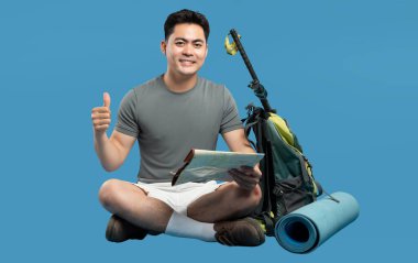 Sırt çantası haritası ve yürüyüş direğinin yanında oturan mutlu yürüyüşçü gülümsüyor Keşfetmeye hazır